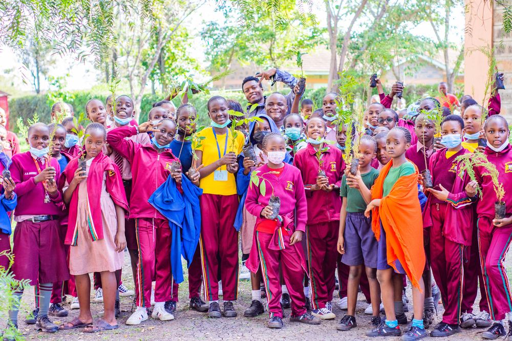 Large group of students and staff holding tree seedlings