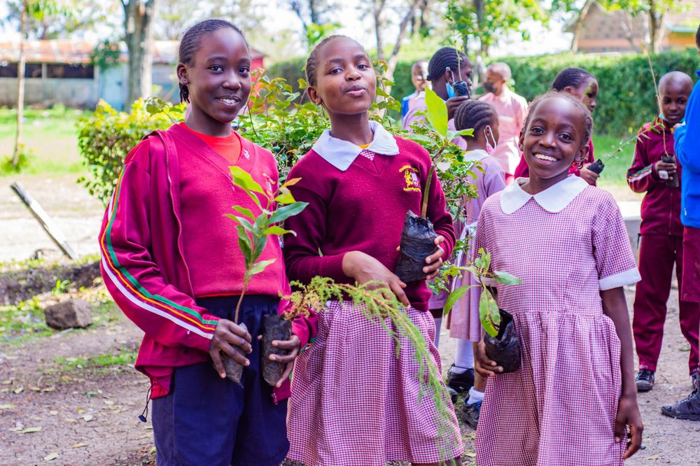 Three students smiling and holding tree seedlings