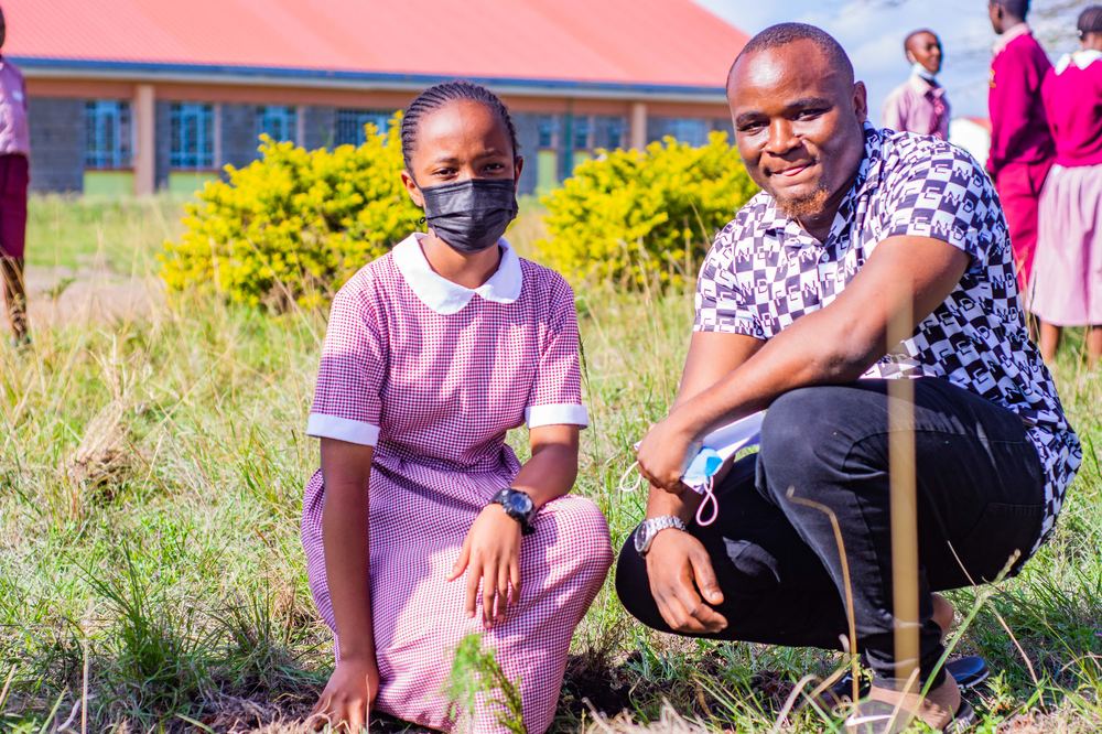 A smiling student kneeling near freshly planted seedlings